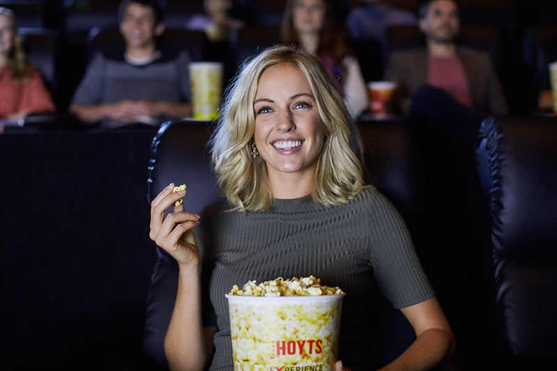 Women smiling and eating popcorn whilst watching a movie at the HOYTS cinema in EntX